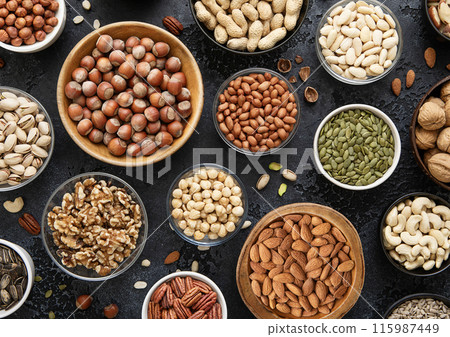 Mixed assorted raw healthy nuts and seeds in various bowls on black kitchen background. 115987449