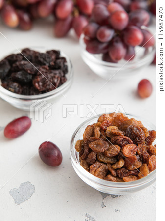 Brown and dark sweet raisins with ripe red grapes on light background. Brown and dark sweet raisins with ripe red grapes on light background. 115987470