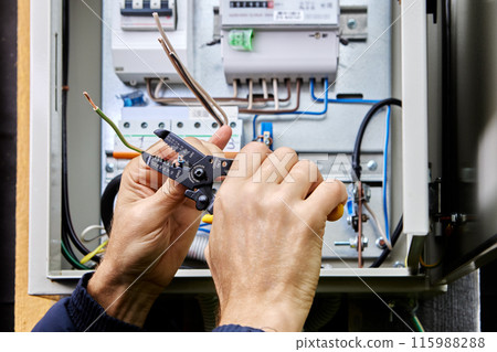 Using stripping and wire cutting tool, an electrician connects three-phase power cable to an outdoor electrical cabinet. 115988288