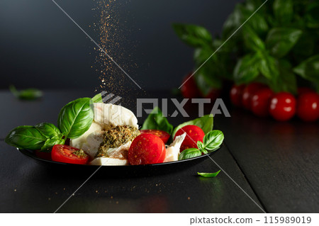 Mozzarella with basil, cherry tomatoes and pesto sauce sprinkled with Mediterranean spices. 115989019