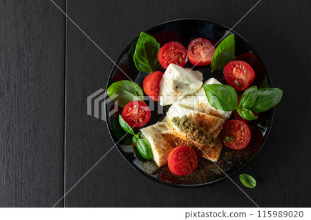 Mozzarella with basil, cherry tomatoes and pesto sauce sprinkled with Mediterranean spices. 115989020