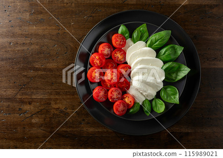 Mozzarella with basil and cherry tomatoes on an old wooden table. 115989021