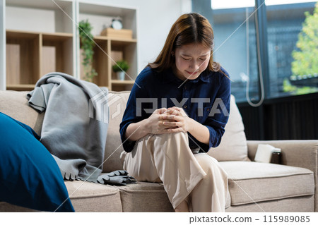 Closeup young woman sitting on sofa and feeling knee pain, Healthcare and medical concept. 115989085