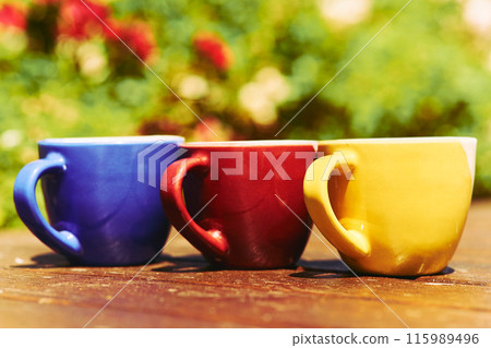 Tea time. Coffee break. Blue yellow red cups on wooden in blooming garden Tea time. Coffee break. Blue yellow red cups on wooden in blooming garden 115989496