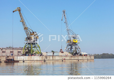 Yellow green portal cranes stand on a quay in harbor Yellow green portal cranes stand on a quay in harbor 115990264