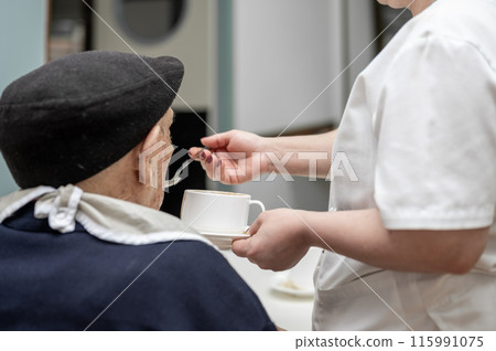 Senior man getting fed by carer in nursing home. 115991075