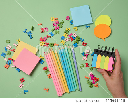 Stationery laid out on a green background. Multi-colored pencils , sticky notes and wooden letters, preparing for study or work Stationery laid out on a green background. Multi-colored pencils , sticky notes and wooden letters, preparing for study or work 115991426