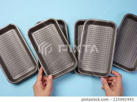 Hand holds black disposable polystyrene foam rectangular plate for packaging vegetables and meat on a blue background 115991443