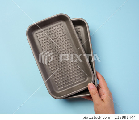 Hand holds black disposable polystyrene foam rectangular plate for packaging vegetables and meat 115991444