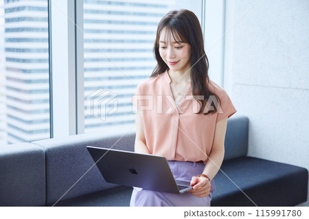Woman looking at a laptop on a sofa in an office 115991780