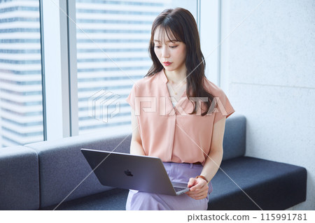 Woman looking at a laptop on a sofa in an office 115991781