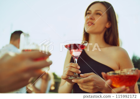 Celebratory vibes fill air as friends clink their glasses, savoring warmth and each other's company. Party outdoor. 115992172