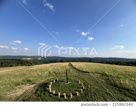 A sundial made of wooden bars in a field among greenery with a beautiful view A sundial made of wooden bars in a field among greenery with a beautiful view 115992349
