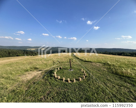 A sundial made of wooden bars in a field among greenery with a beautiful view 115992350