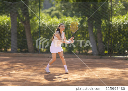 A woman is playing tennis on a clay court A woman is playing tennis on a clay court 115993480