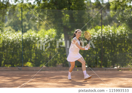 A young woman is playing tennis on a clay court A young woman is playing tennis on a clay court 115993533