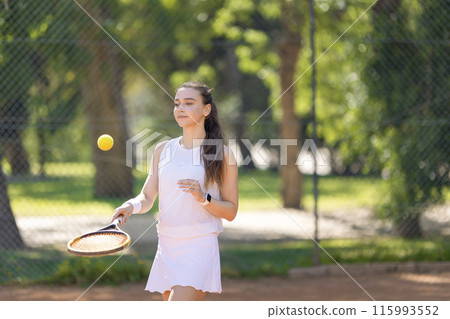 A woman is playing tennis with a tennis ball A woman is playing tennis with a tennis ball 115993552