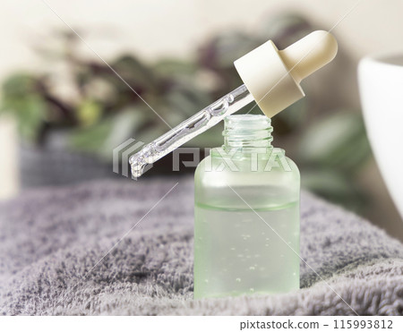 Droplet falls from a pipette set on a glass bottle filled with green liquid on grey towel Droplet falls from a pipette set on a glass bottle filled with green liquid on grey towel 115993812