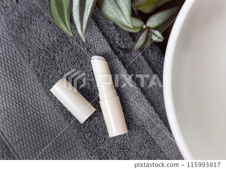 Opened lip balm stick on grey towels near green plant and vessel basin in bath, lid mockup Opened lip balm stick on grey towels near green plant and vessel basin in bath, lid mockup 115993817