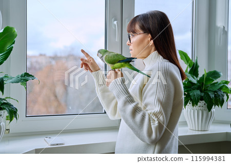 Middle aged woman and parrot together at home, near winter window 115994381