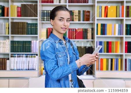 Teenage female student using smartphone, inside high school building, in library 115994859