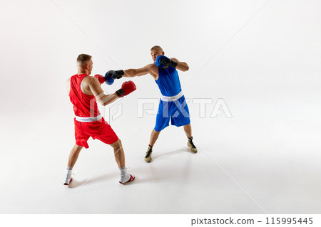 Two skilled fighters, boxers in blue and red attire, in high-energy sparring match to enhance their abilities against white studio background. Two skilled fighters, boxers in blue and red attire, in high-energy sparring match to enhance their abilities against white studio background. 115995445
