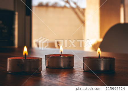 Small burning candles placed against window  115996324