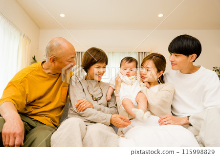 A family of 5 in 3 generations of parents and grandparents watching over a 0-year-old baby in the living room 115998829