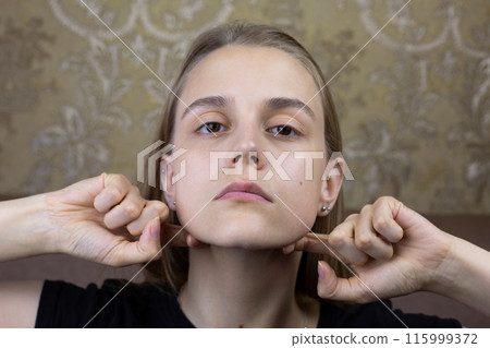 Young girl smooths out wrinkles on her face with hands with special oil for massage, beauty procedure of European girl for body skin care 115999372
