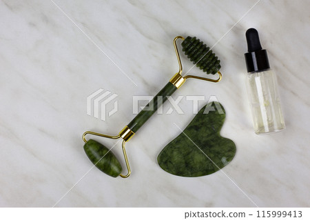 Facial massage and skin care set with special gua sha scraper, moisturizing oil and wrinkle smoothing stone roller lies on white table 115999413