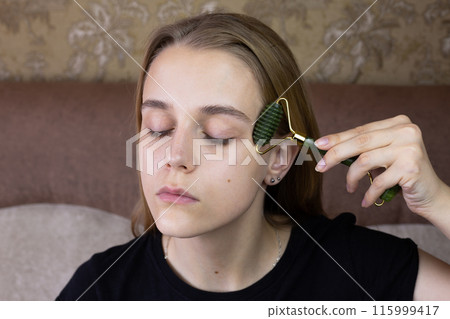 Young European girl makes facial massage using stone roller to smooth out wrinkles and take care of body skin for beauty Young European girl makes facial massage using stone roller to smooth out wrinkles and take care of body skin for beauty 115999417