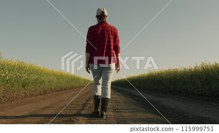 Business Woman Farmer In Rubber Boots Walks Along A Country Road Near A Green Field Of Rapeseed Field. Farmer Boots And Legs Treading Country Road. Business Woman Farmer In Rubber Boots Walks Along A Country Road Near A Green Field Of Rapeseed Field. Farmer Boots And Legs Treading Country Road. 115999751