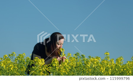 Woman Standing Along A Rapeseed Field And Touches Flowers Of Rapeseed With Her Hand. Portrait Of Attractive Rural Woman. 115999796