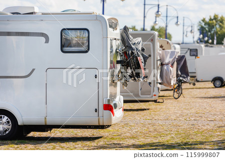 Many white modern campervan recreational motor home vehicles parked in row at camper park site Magdeburg city against Elbe river bridge. Motorhome campground stataion travel destination. RV lifestyle 115999807