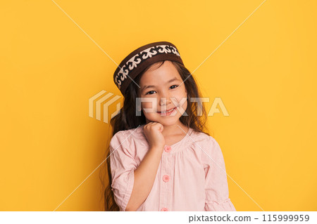 Child in a Kazakh skullcap in front of a yellow background Child in a Kazakh skullcap in front of a yellow background 115999959