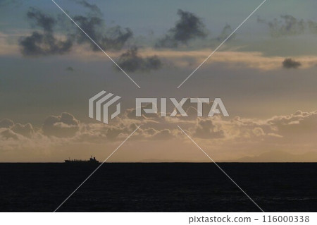 The sun is setting and the sea is dark; the silhouette of a ship sailing in the distance The sun is setting and the sea is dark; the silhouette of a ship sailing in the distance 116000338