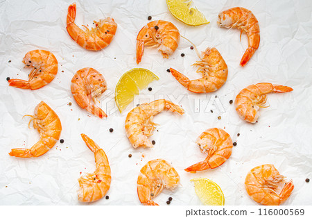 Roasted or grilled shrimps with seasonings and fresh lemon wedges top view on baking paper, healthy snack or appetizer. Seafood barbecue 116000569