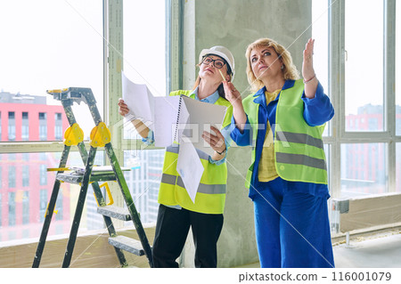 Two female industrial workers at construction site discussing work plans 116001079