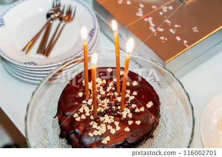 Chocolate cake with four burning candles on a white table. Chocolate cake with four burning candles on a white table. 116002701