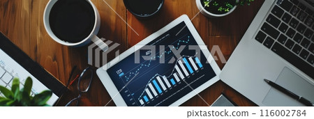 Overhead view of a digital tablet with financial graphs on a desk with coffee and a laptop. Business strategy and modern workspace setting. 116002784