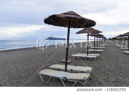 Empty beach with sun loungers and umbrellas in the early morning and a cloudy sky. Crete Greece. 116002785