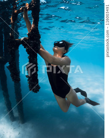 Freediver in blue sea holding on to the stairs. Female freediver underwater Freediver in blue sea holding on to the stairs. Female freediver underwater 116003491