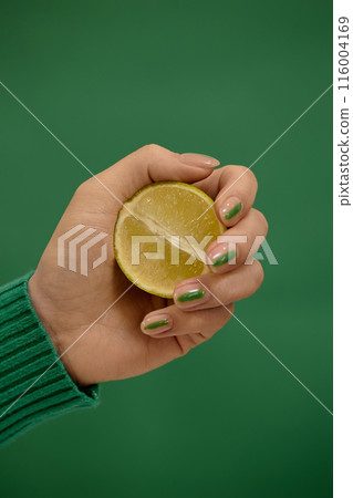 Vertical side view of half lime in womans hand with minimalistic manicure matching fresh fruit in color on emerald green background, copy space Vertical side view of half lime in womans hand with minimalistic manicure matching fresh fruit in color on emerald green background, copy space 116004169
