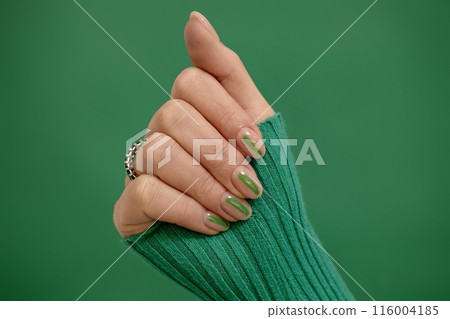 Studio single color shot of neat short almond shaped nude fingernails decorated with green streak on emerald background, copy space 116004185