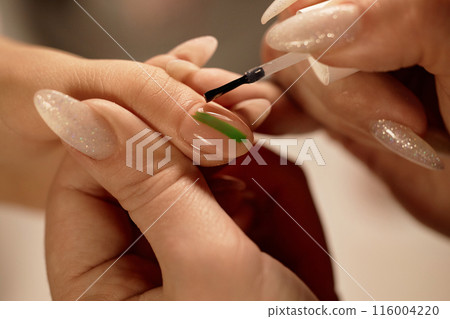 Close up on nail techs work with transparent top coat as final layer on manicure with abstract line design, copy space 116004220