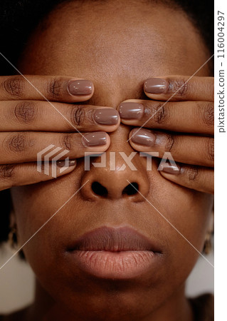 Vertical extreme close up on young Black woman covering eyes with hands in fear feeling hurt. Female African American experiencing abuse in relationship 116004297
