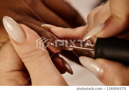 Close up on clients nail with dark brown polish. Manicurist covering nails with monochrome lacquer in salon, focus on nail, copy space 116004378