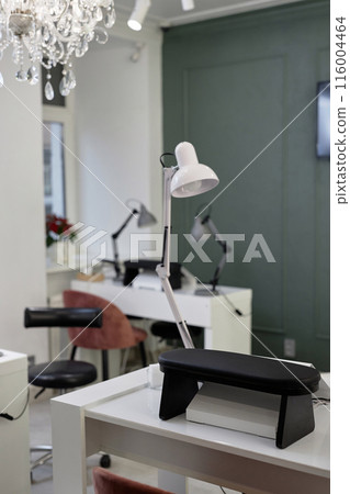 Vertical shot of manicure workplace with white table lamp. Modern bright interior design of nail salon with professional equipment, focus on lamp Vertical shot of manicure workplace with white table lamp. Modern bright interior design of nail salon with professional equipment, focus on lamp 116004464