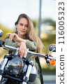 Beautiful Caucasian biker-woman posing on her bike after driving and looking at camera. 116005323