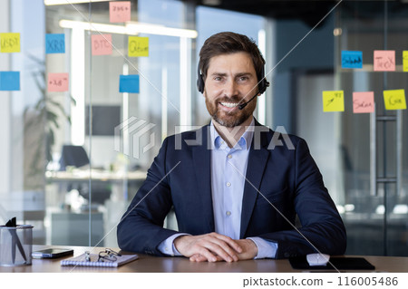 Confident businessman wearing headset smiling during video call in modern office. Concept of business communication, support, and modern workplace. 116005486